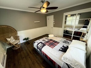 Ein Schlafzimmer mit Bett, Deckenventilator, Korbsessel, Fenster und Kleiderschrank.