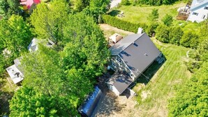 Ein Luftbild eines Hauses, das von Bäumen umgeben ist, mit sichtbarer Garage und blauem Himmel.