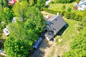 Ein Luftbild eines Hauses, das von Bäumen umgeben ist, mit sichtbarer Garage und blauem Himmel.