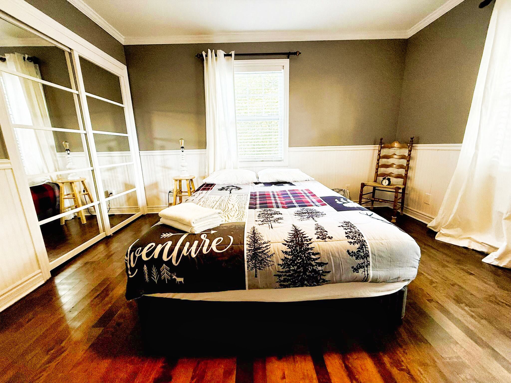 A bedroom with a bed, a window with curtains, a chair, and a shelf.