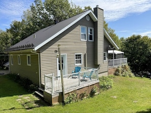 Une maison à deux étages avec un porche couvert, une cheminée et une petite terrasse avec des chaises.
