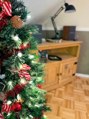 Un arbre de Nadal amb ornaments i llums, un escriptori amb una làmpada, i terres de fusta.