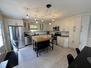 A modern kitchen with stainless steel appliances, white cabinetry, a wooden island, and pendant lighting. - 4-Bedroom Family Retreat · Lake Access · Fireplace · Mandeville, Lanaudière (Mandeville)