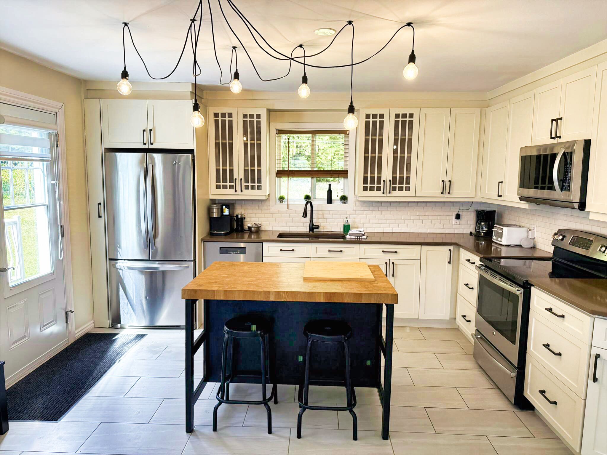A modern kitchen with white cabinets, stainless steel appliances, a wooden island with bar stools, and pendant lighting.