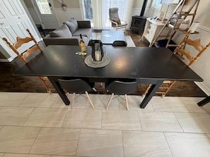 Un coin repas avec une table noire, quatre chaises, une bouteille de vin et un set de table en fibres tressées.