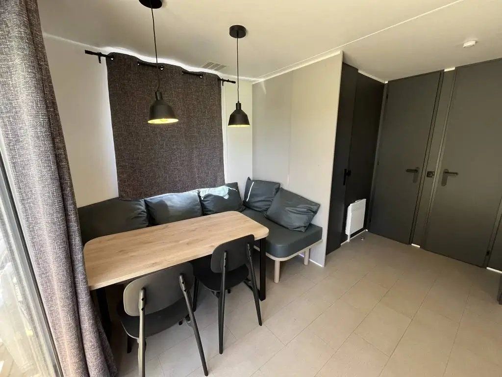 A modern living space with a sofa, a dining table, and chairs. There is a large wardrobe and a radiator on the wall.