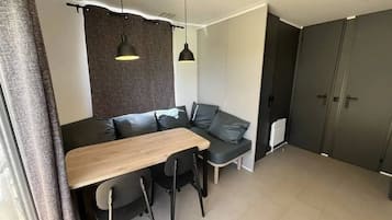 A modern living space with a sofa, a dining table, and chairs. There is a large wardrobe and a radiator on the wall.