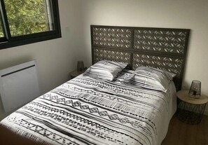 Een bed met een beddengoed met een patroon, een hoofdbord met een geometrisch ontwerp en een nachtkastje met een lamp.