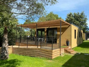 A wooden cabin with a covered patio, outdoor seating, and a fenced area. - Chalet - Piscine - ccbfiia (Bollène)