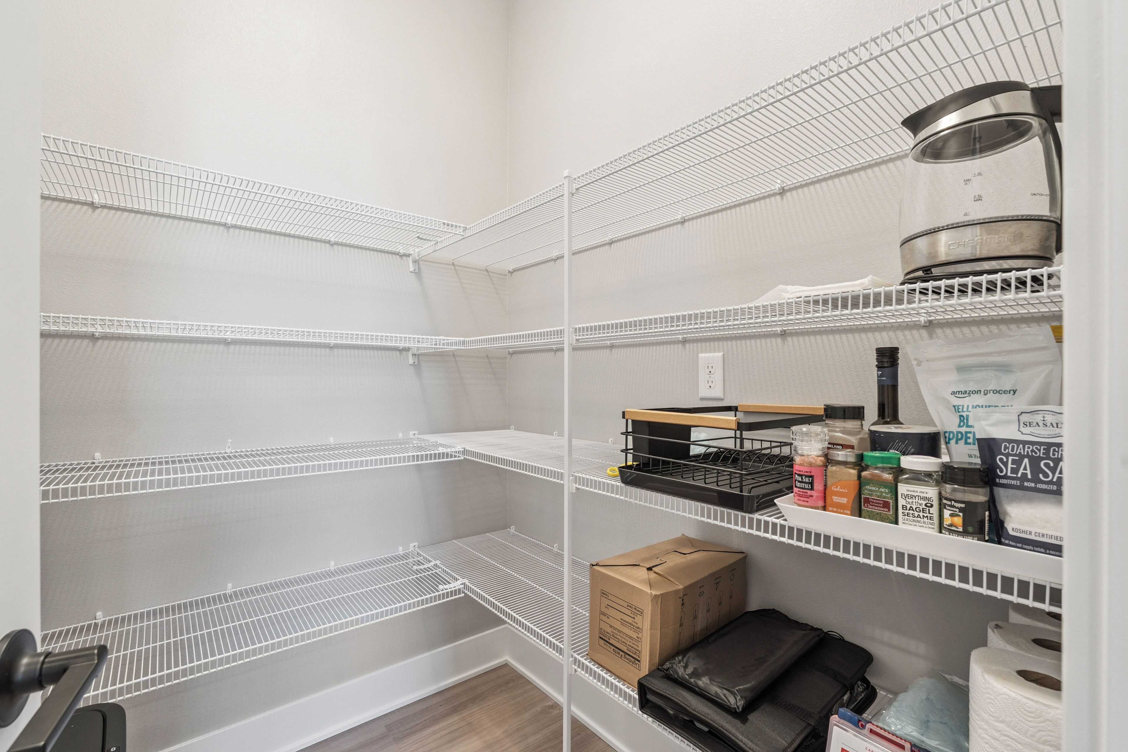 Un espace de stockage équipé d’étagères métalliques, d’une bouilloire et de divers produits emballés.