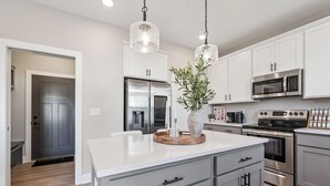 Una cocina moderna con electrodomésticos de acero inoxidable, armarios blancos e iluminación colgante.