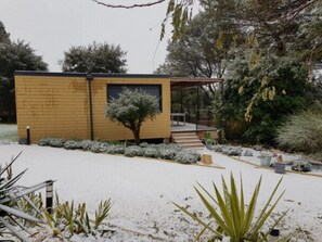 En modern byggnad med en fasad av tegel, en överbyggd entré och en snötäckt trädgård med olika växter.