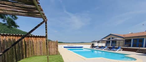 Una piscina con una valla de madera, una zona techada y un edificio con tejado de baldosas.