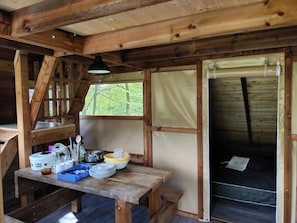 Ein Holzblockhaus-Interieur mit Esstisch, Bett und Fenster mit Blick auf Grünflächen.