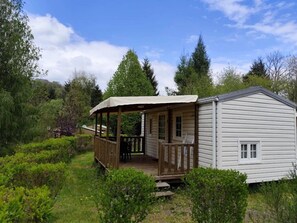 Eine eingeschossige Hütte mit Veranda, umgeben von Grünpflanzen und Bäumen.