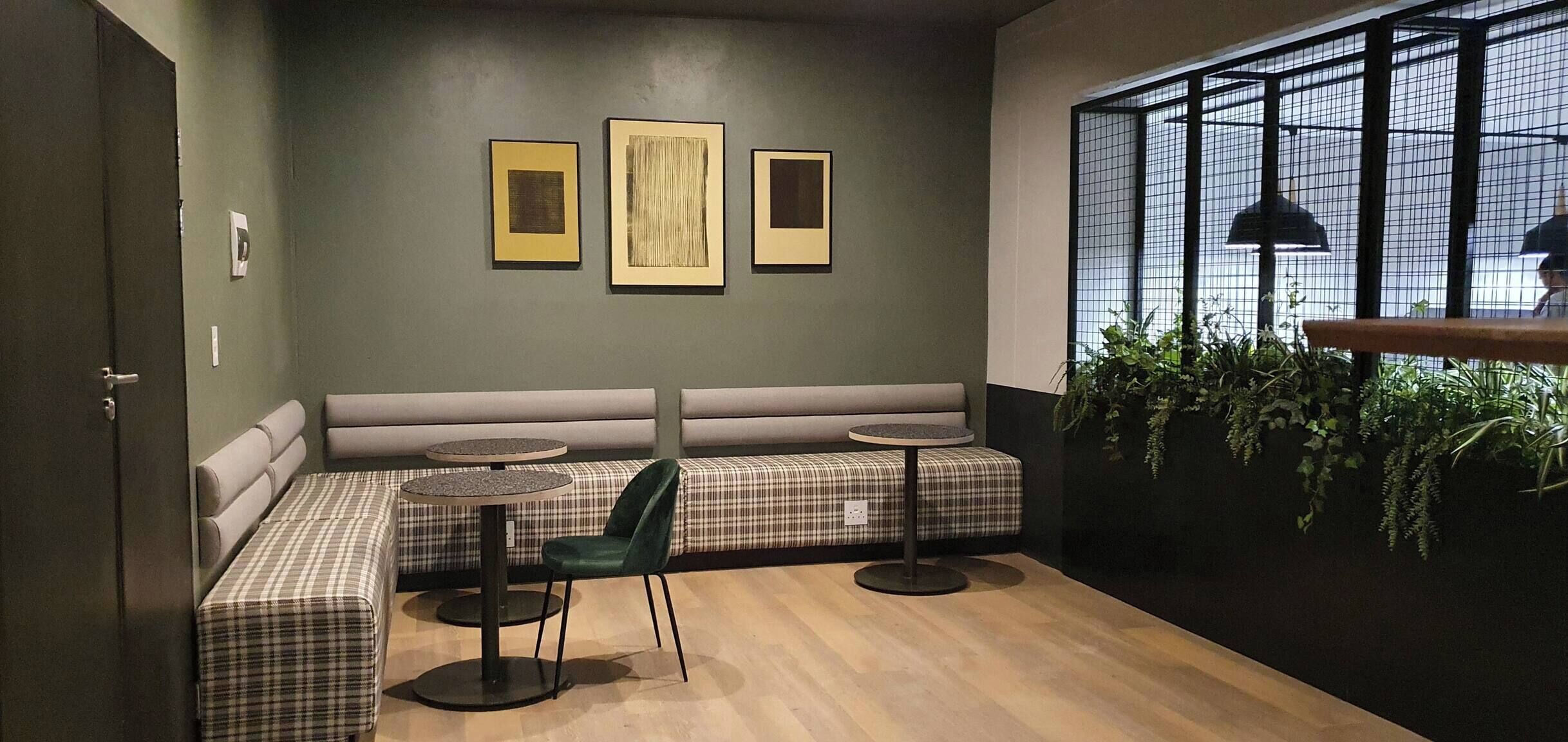 A seating area with a bench and round tables, a wall with framed artwork, and a window with plants.