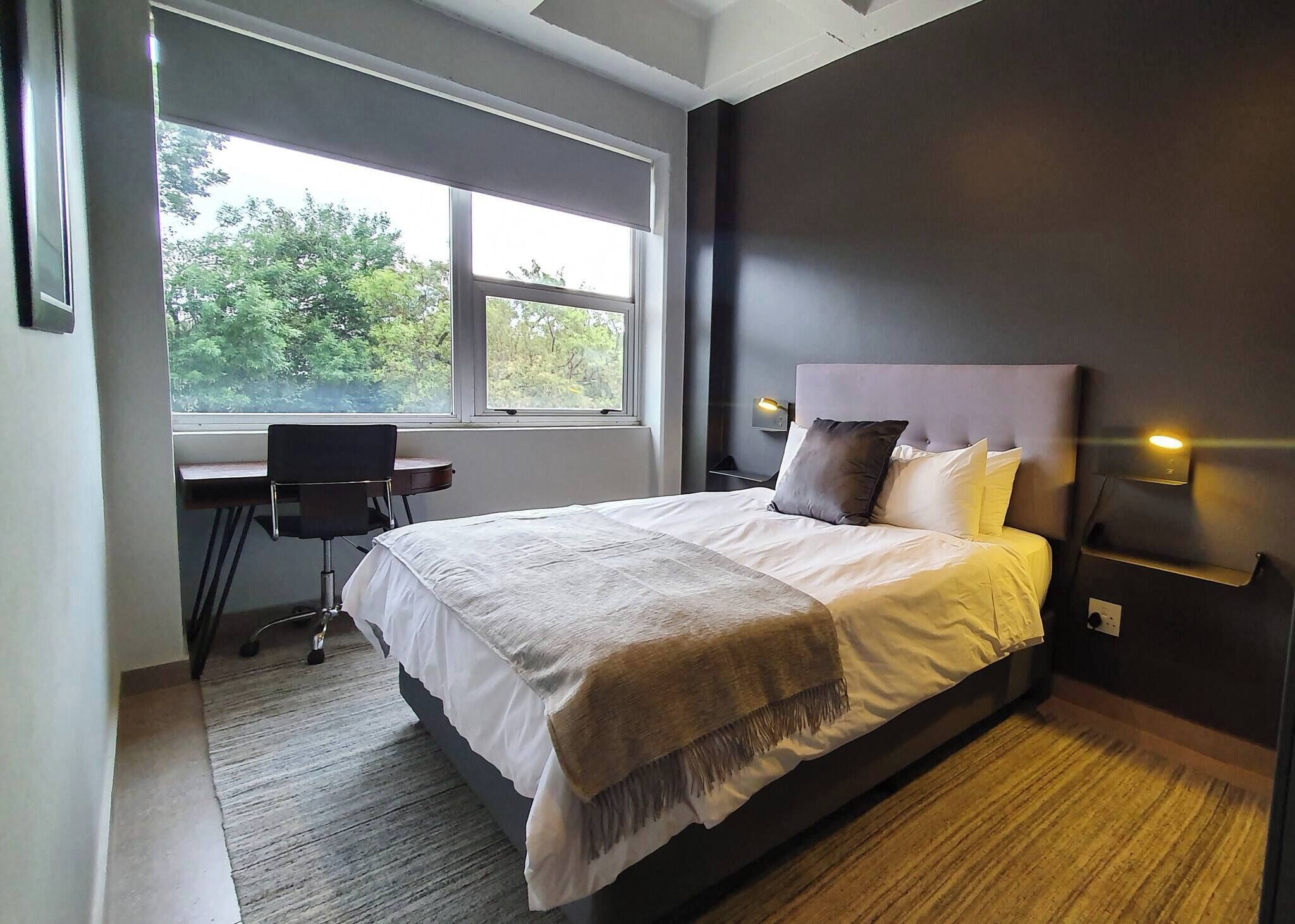 A bedroom with a bed, a desk, and a window.