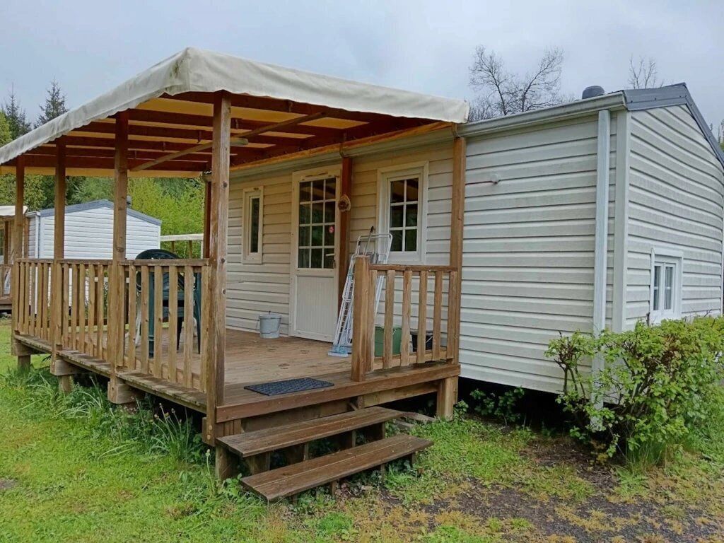 Une cabane en bois d’un seul étage, dotée d’une véranda, d’un espace abrité et d’un petit abri attenant.