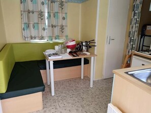 Ein gemütlicher Raum mit einem grünen Sofa, einem kleinen Tisch mit Küchenutensilien, einem Fenster mit Vorhängen und einem Waschbecken.