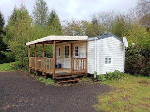 Eine kleine Holzhütte mit Veranda, Satellitenschüssel und einem Schotterweg.