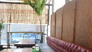 An outdoor seating area with a wooden table, a cushioned bench, and a bamboo ceiling. - Aquí Comes Rico Airport Hostel (Mexico City)