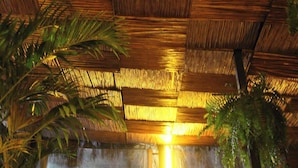 A room with a bamboo ceiling, a large window, and various indoor plants. - Aquí Comes Rico Airport Hostel (Mexico City)