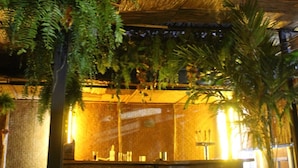 A room with a thatched roof, a bench, and a table with chairs. - Aquí Comes Rico Airport Hostel (Mexico City)