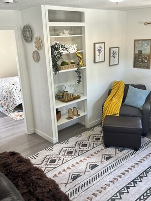 A living room with a sofa, a patterned rug, a white shelving unit with decorative items, and a door leading to another room. - Rood Roost: Spacious 3BR Near Downtown & Grand Junction Adventures (Grand Junction)