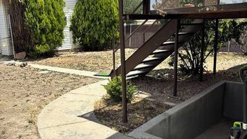 A concrete pathway leading to a metal staircase with a mesh enclosure, surrounded by a yard with sparse grass and a few trees.