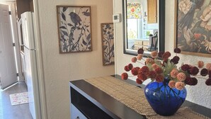 Un couloir avec une commode noire, un vase bleu rempli de fleurs et des œuvres d’art encadrées accrochées aux murs.