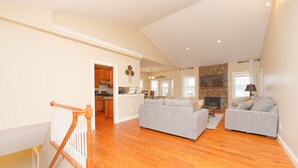 A spacious living area with hardwood flooring, two grey sofas, a kitchen in the background, and a staircase with wooden railings. - Gorgeous Views of Round lake (Round Lake)