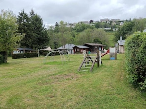 Eine grüne Grünfläche mit Spielgeräten, einer Holzleiter und Häusern im Hintergrund.