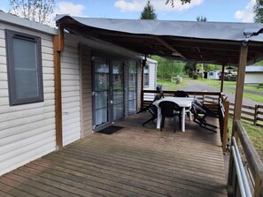 Eine überdachte Terrasse mit Tisch und Stühlen, eine Schiebetür und Blick auf eine Wohngegend.