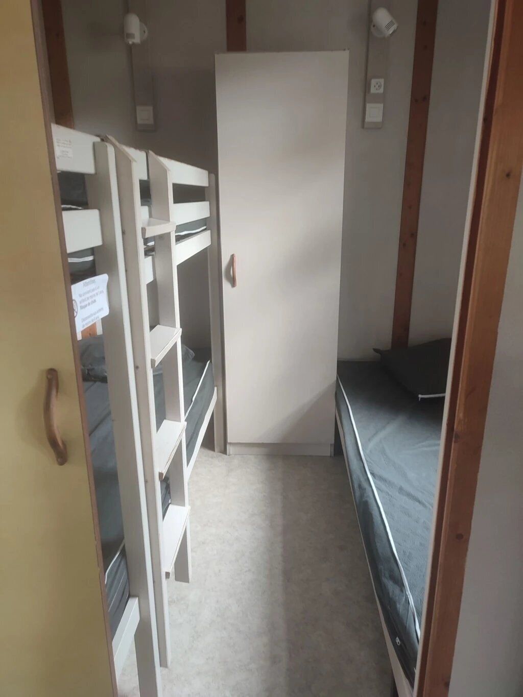 A small room with a bunk bed, a white door, and a shelving unit with storage boxes.