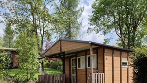 Eine kleine Holzhütte mit Veranda, umgeben von einer Wiese und Bäumen.