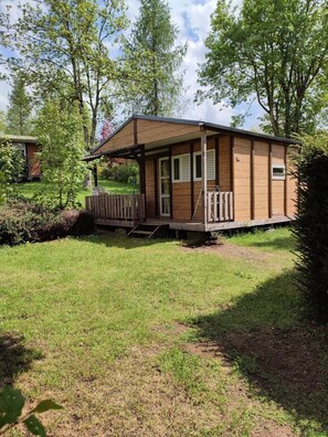 A small wooden cabin with a porch, surrounded by a grassy area and trees. - Chalet 2 étoiles - ccbgafb (La Tour-d'Auvergne)