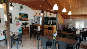 Ein Restaurant mit hohen Holzbalkendecken, mehreren Tischen und Stühlen, einer Küchenzeile und Wanddekorationen.