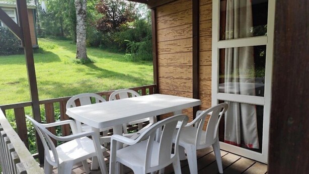 Ein überdachter Außenbereich mit Tisch und Stühlen, einer Holzterrasse und Blick auf eine Rasenfläche.