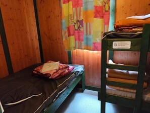Et lille værelse med en enkelt seng og en træhusseng langs væggen, et farverigt gardin og et skilt med en advarsel.