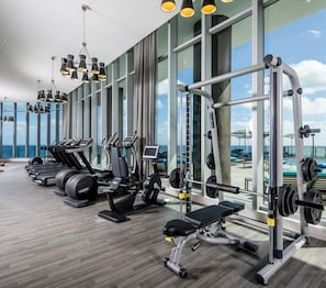 A gym with cardio machines, weightlifting equipment, and large windows offering a view of the ocean. - Lyfe 2-bedroom apartment over the beach great view (Hollywood)