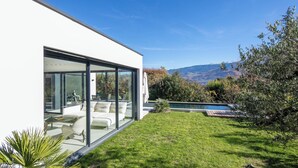 Ein modernes Haus mit Glasfassade, einem Pool und Blick auf Berge.