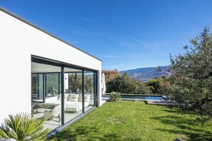 Ein modernes Haus mit Glasfassade, einem Pool und Blick auf Berge.