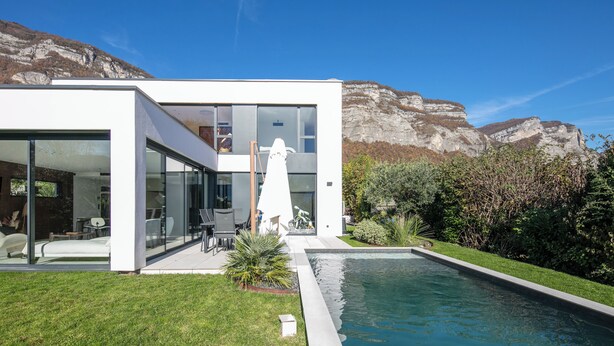 Ein modernes Haus mit Swimmingpool, großen Glasfenstern und Bergblick.