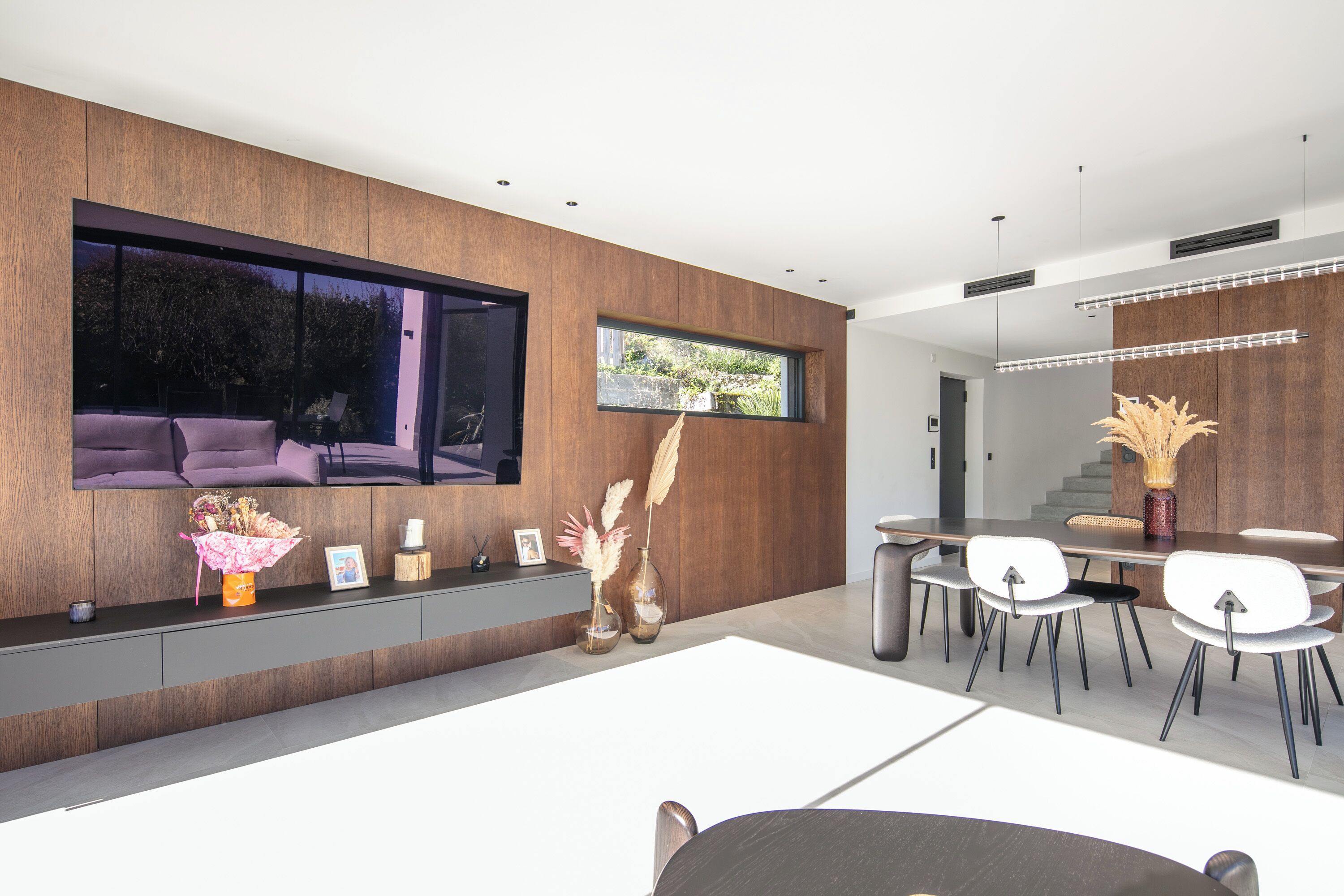 A modern interior with a dining area, a large window, and a flat-screen TV mounted on the wall.
