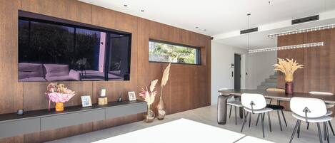 A modern interior with a dining area, a large window, and a flat-screen TV mounted on the wall.