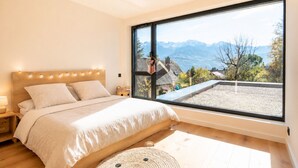 Ein Schlafzimmer mit großem Fenster, einem Bett mit Holz-Kopfteil und Bergblick.