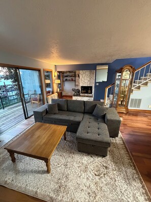 A modern living room with a sectional sofa, a wooden coffee table, a fireplace, and a staircase. - Riverfront Retreat - Waterfront Views & 2 Decks (Portland)