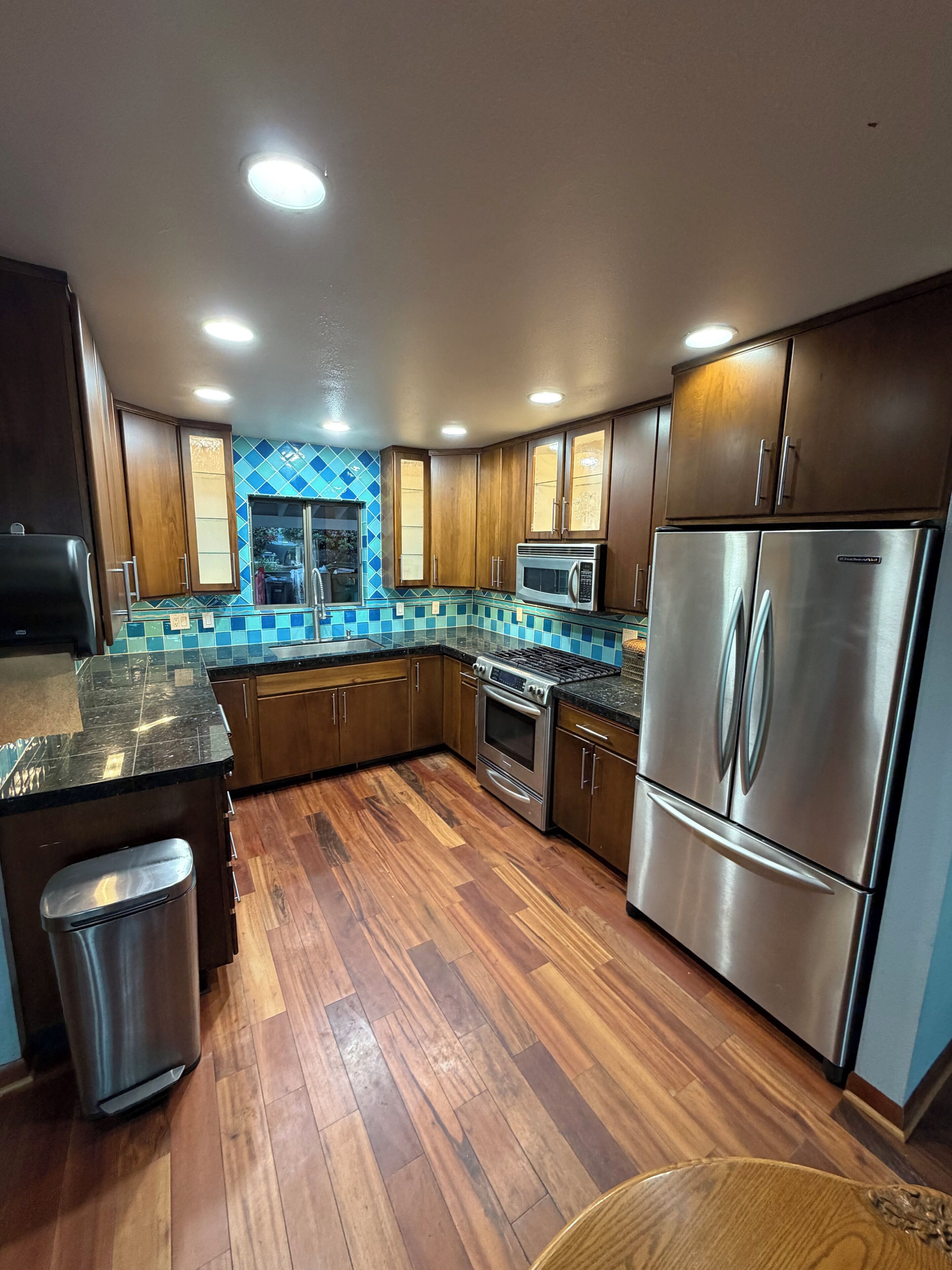 A modern kitchen with wooden cabinets, stainless steel appliances, and a blue-tiled backsplash.