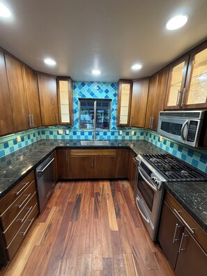 A kitchen with wooden cabinets, a stainless steel microwave, and a tiled backsplash. - Riverfront Retreat - Waterfront Views & 2 Decks (Portland)