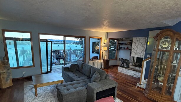 A spacious living room with a large sectional sofa, a wooden dining table, and a view of a dock and water. - Riverfront Retreat - Waterfront Views & 2 Decks (Portland)